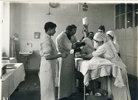 L1 Operation room on the front shell splinters in the buttock In an operating room, a man lies on his side on a narrow table surrounded by two women and four men
