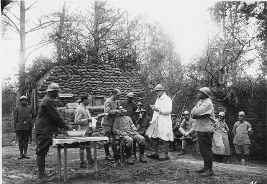 Monaco near Chemin des Dames Sept. 1917 A man sits on a chair outdoors while the man standing behind him places two dental tools in his open mouth. A dental machine powered by